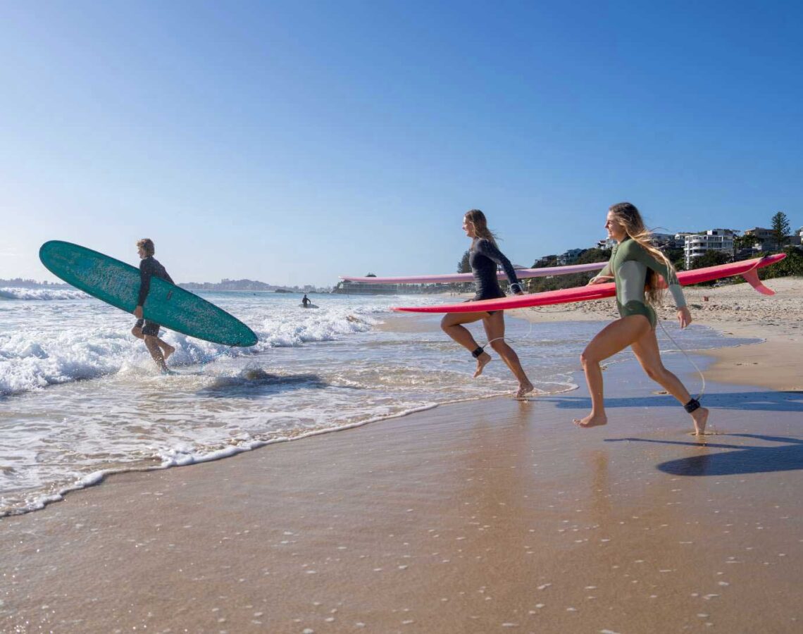 Three people run with surfboards into the ocean.