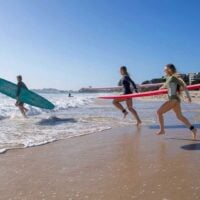Three people run with surfboards into the ocean.