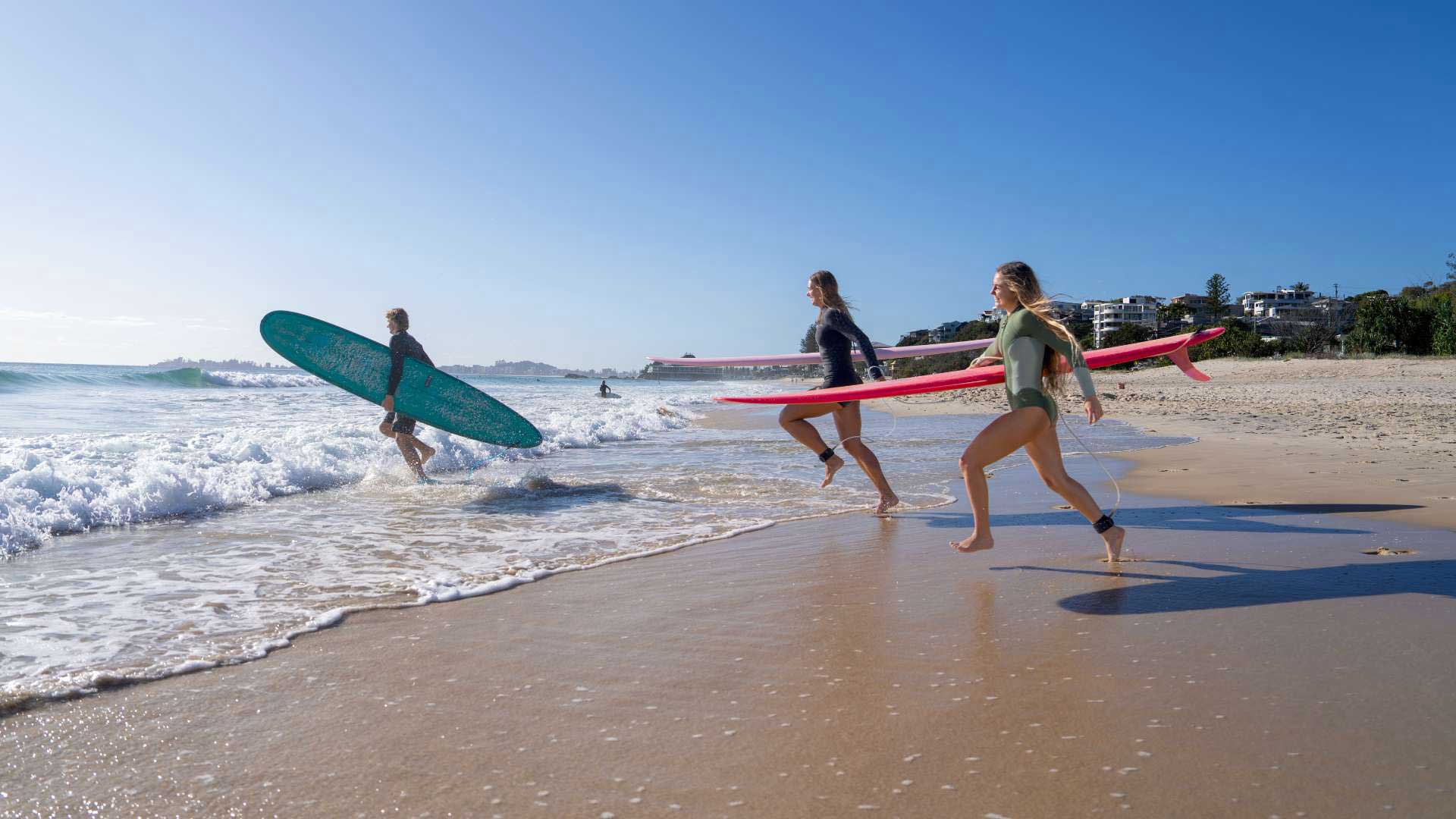 Three people run with surfboards into the ocean.