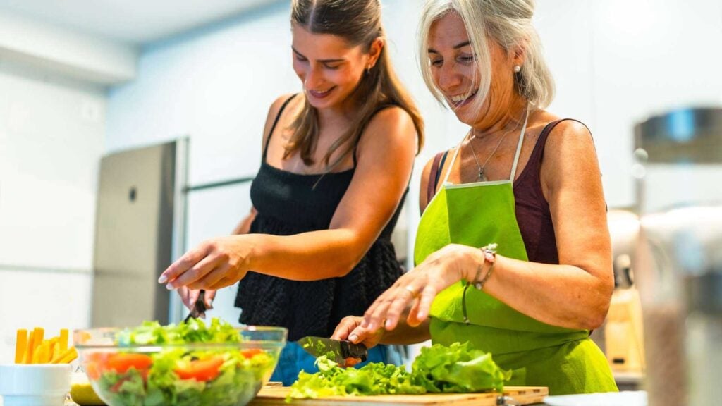 Mother and daughter enjoying making healthy leafy salad in the kitchen