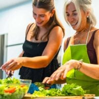 Mother and daughter enjoying making healthy leafy salad in the kitchen