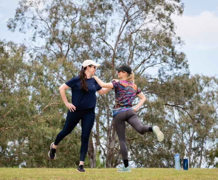 Two people stretching outside, wearing caps.
