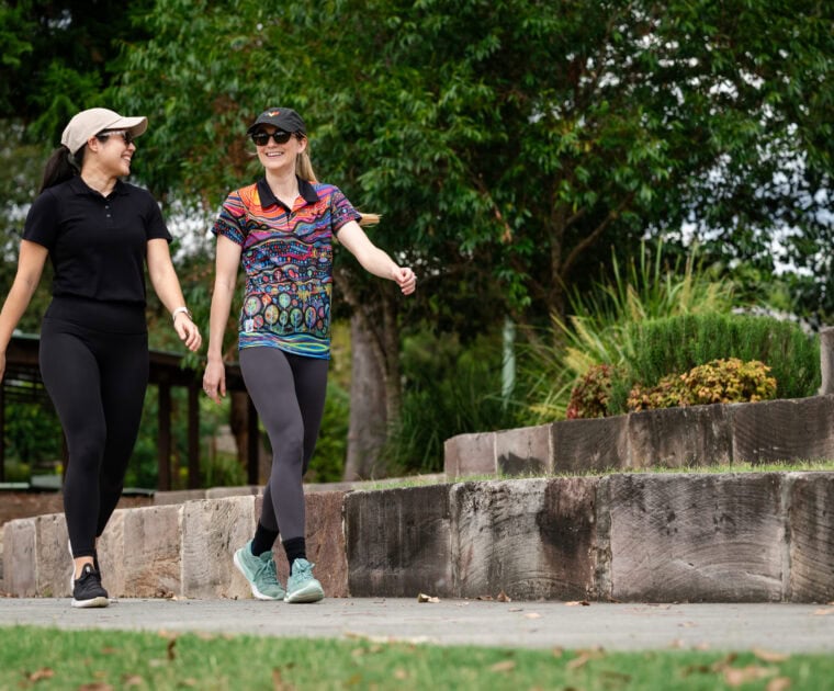 Two people wearing hats and active clothing going for a walk outside, smiling.