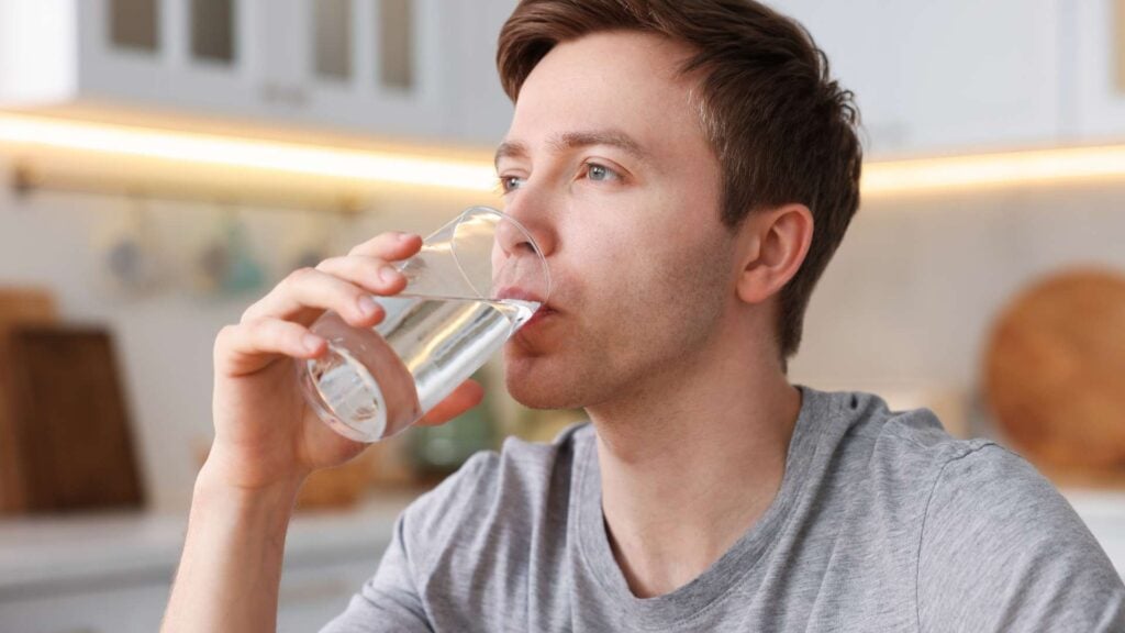 Young man drinking a glass of water in the kitchen