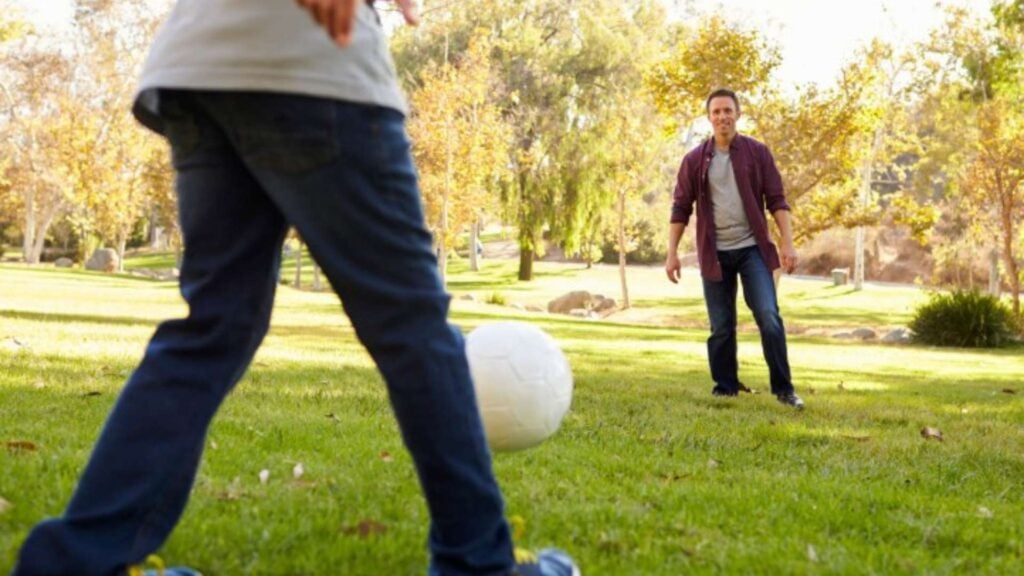 Father and child kicking a soccer ball in the park