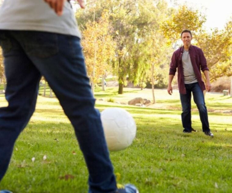 Father and child kicking a soccer ball in the park
