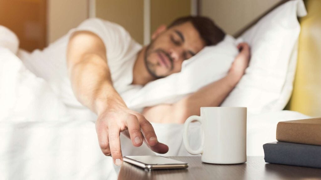 Man laying in bed reaching for phone