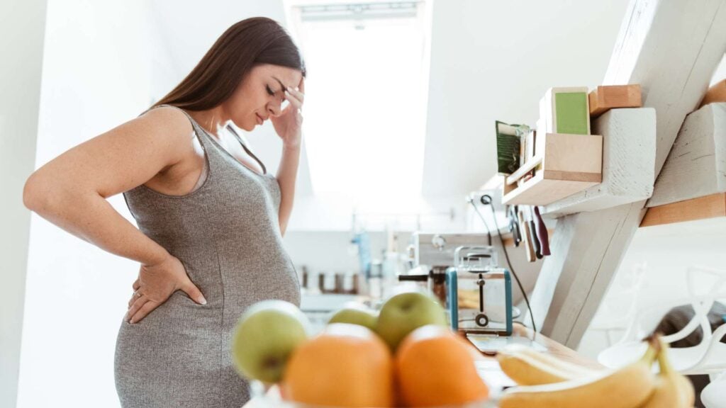 Pregnant women looking stressed standing in kitchen