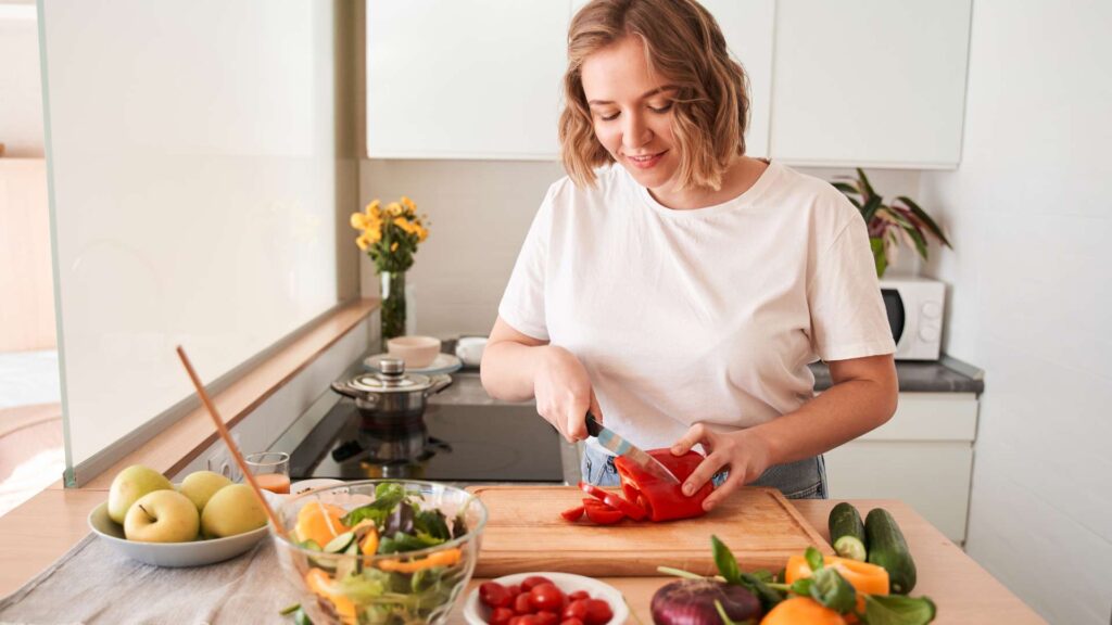 Woman in kitchen chopping up vegetables and preparing salad