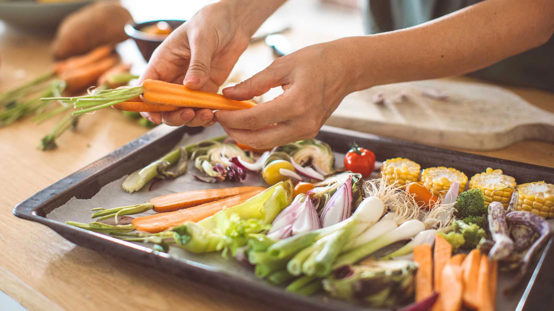 Person arranging a variety of vegetables on roasting tray