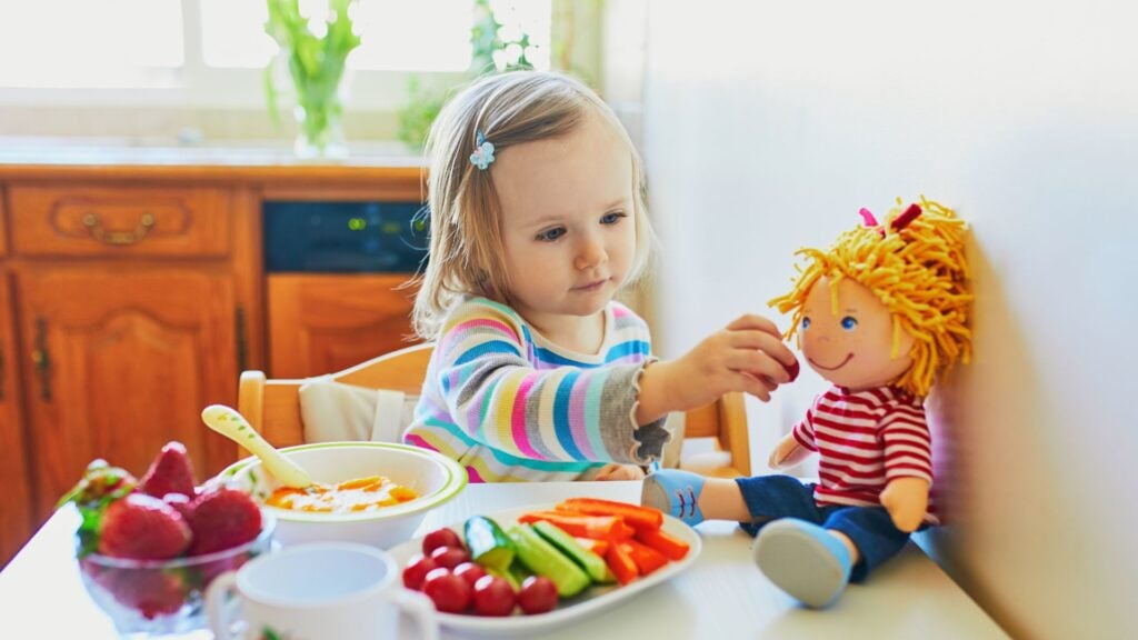 Young girl feeds her dolly a healthy snack