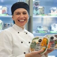 Chef with healthy meal options stands in front of cafeteria fridge