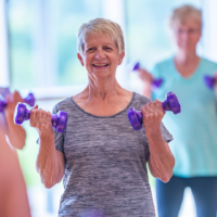 Woman standing in a exercises class holding two purple weights.
