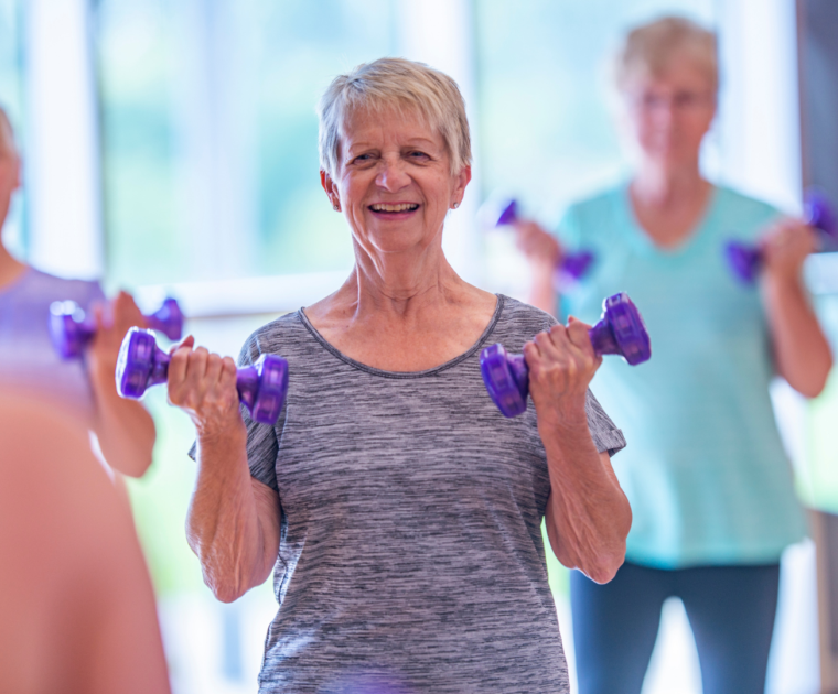 Woman standing in a exercises class holding two purple weights.
