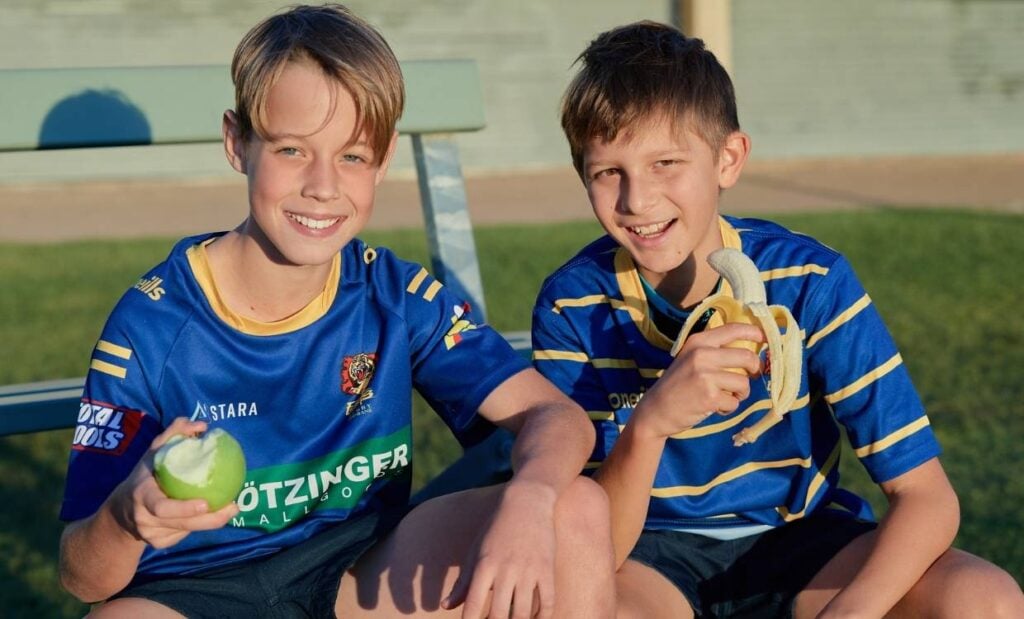 Two young rugby players eating fruit on the sidelines