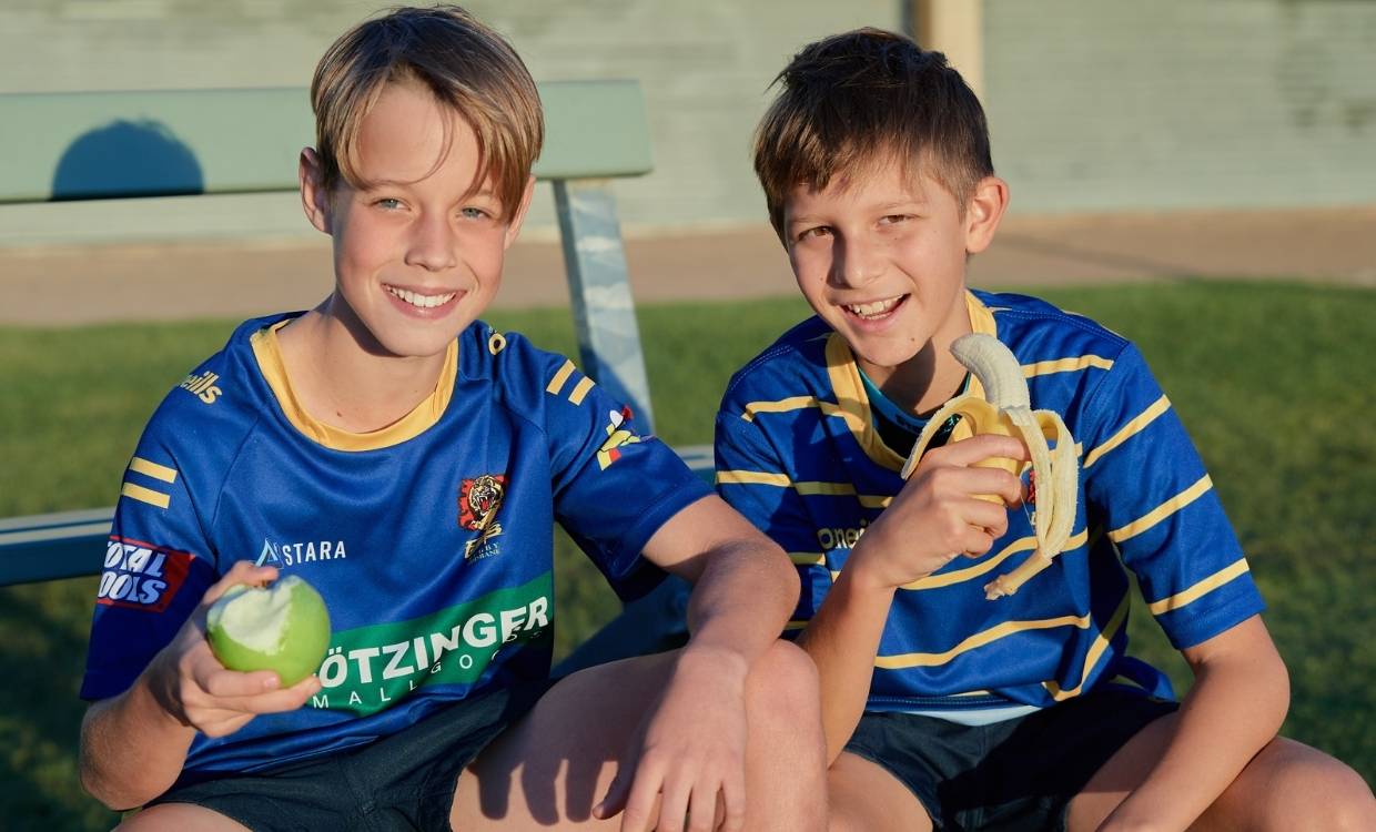 Two young rugby players eating fruit on the sidelines