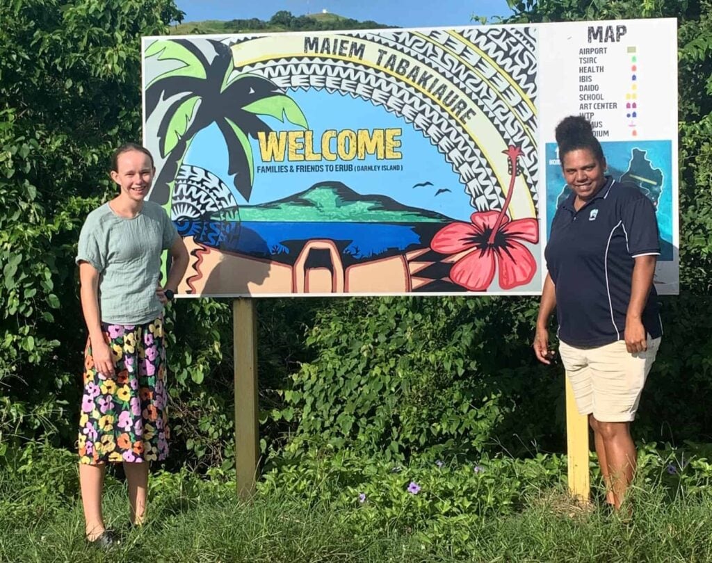 two women standing in front of a 'Welcome to Darnley Island' sign