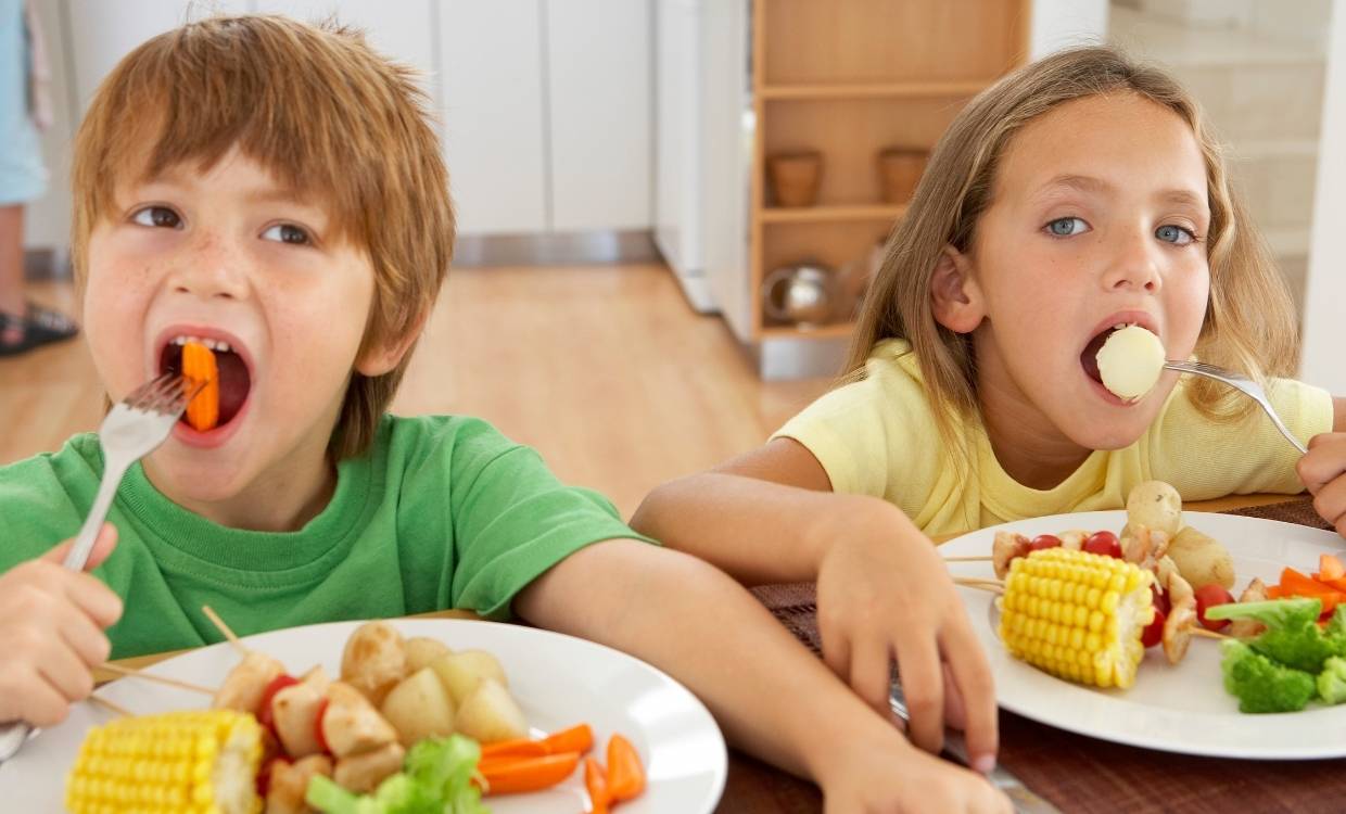 Two children eat vegetables from their plates