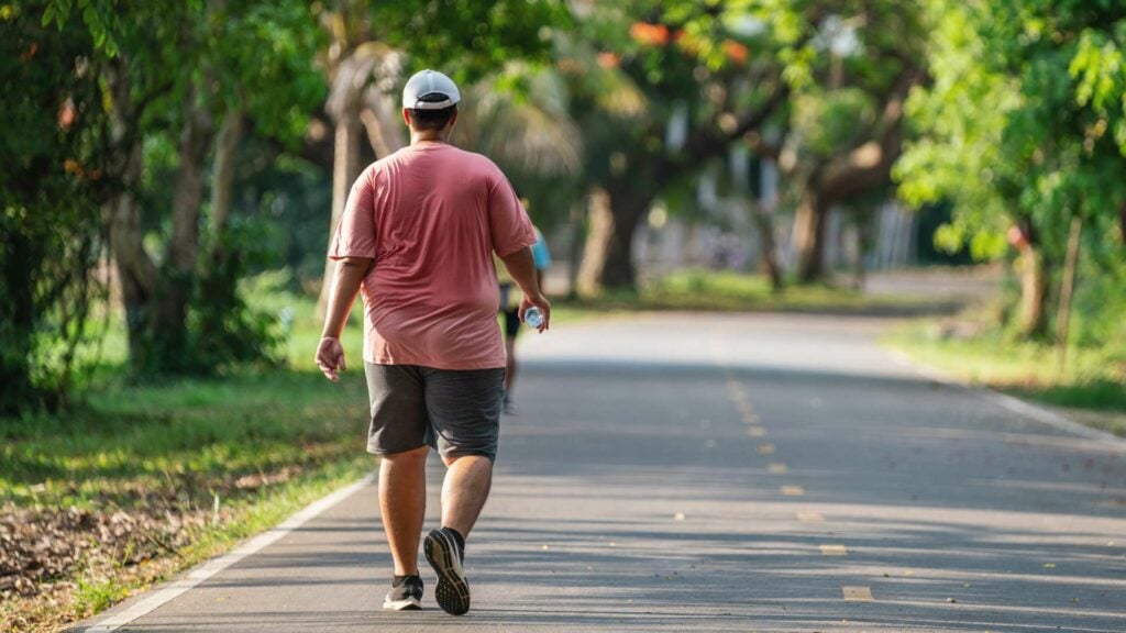 Man carrying water bottle walking outside with cap on.