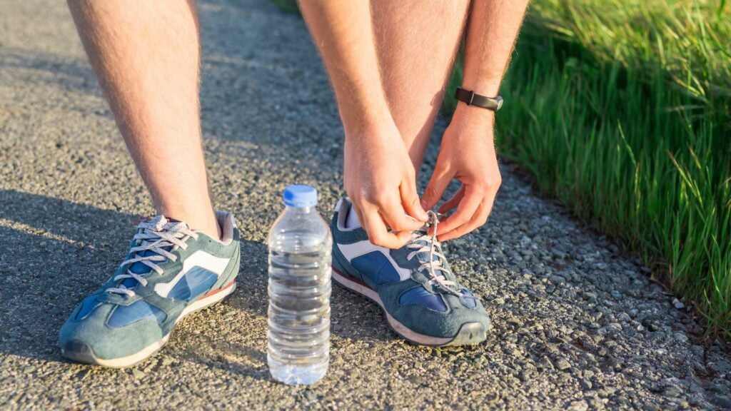 Person tying up running shoes with water bottle on ground.