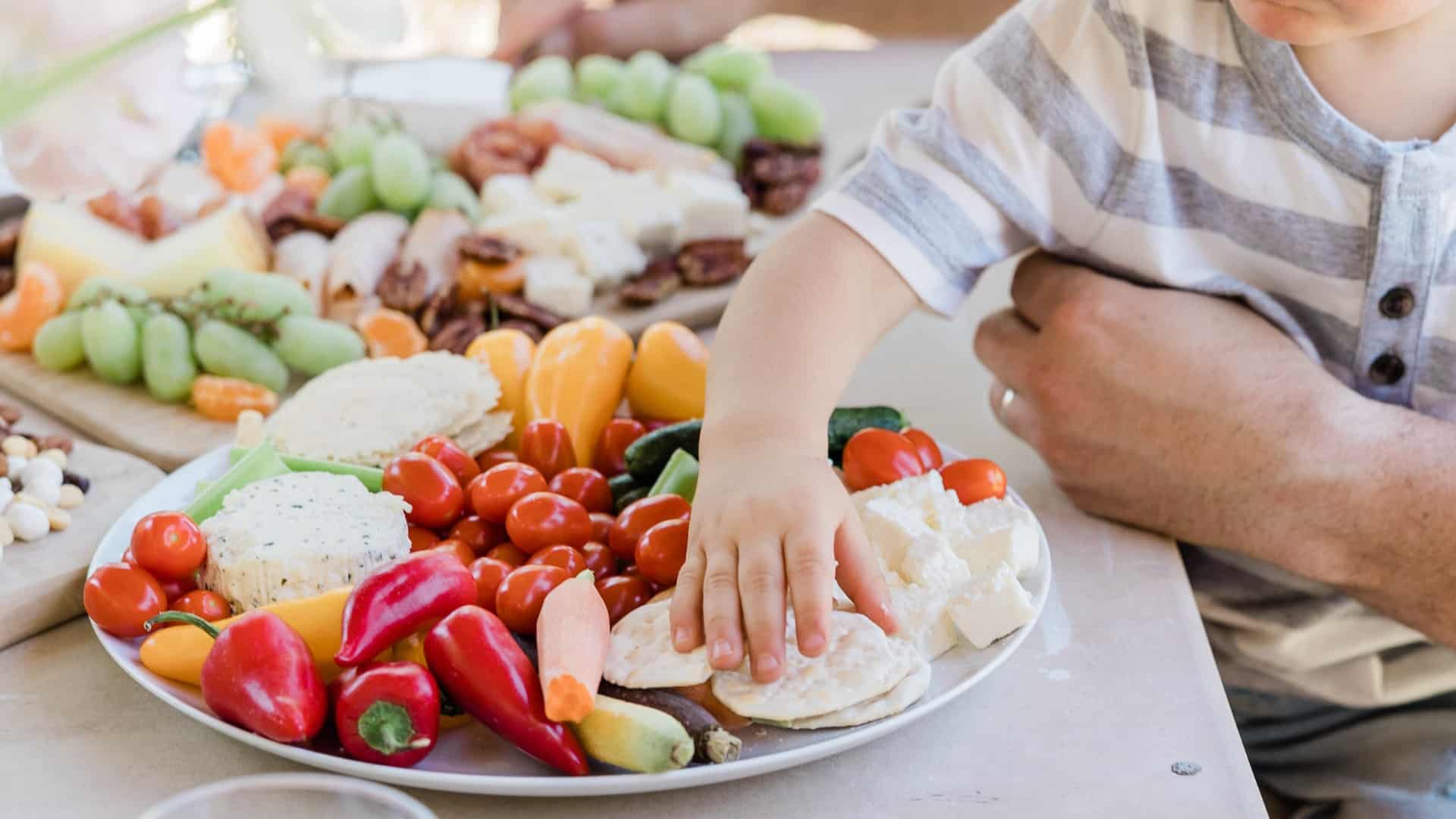A toddler reaches for a cracker on a veggie platter