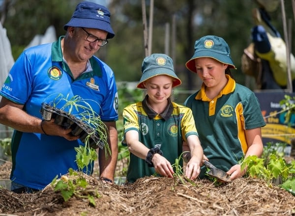 Two students with teacher planting vegetables in the school garden as part of the Pick of the Crop program