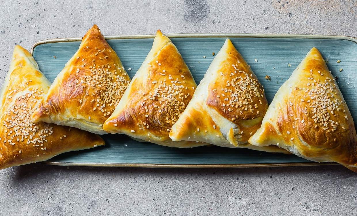 A plate of triangle pastries sprinkled with sesame seeds