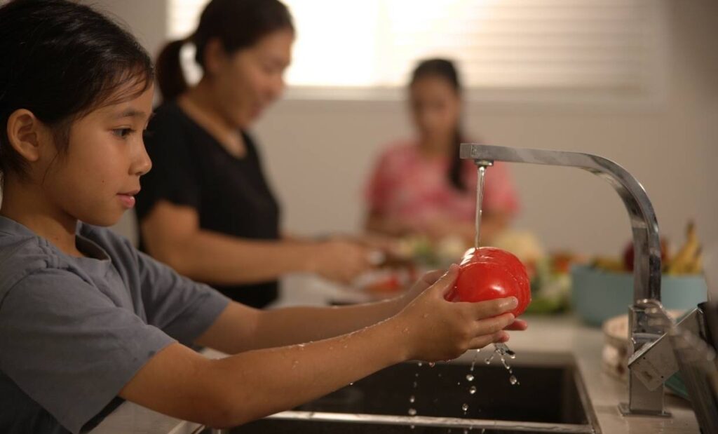 Child washes red capsicum under the kitchen tap