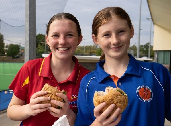 Two happy girls wearing sports club uniforms, eating healthy burgers outside the club canteen