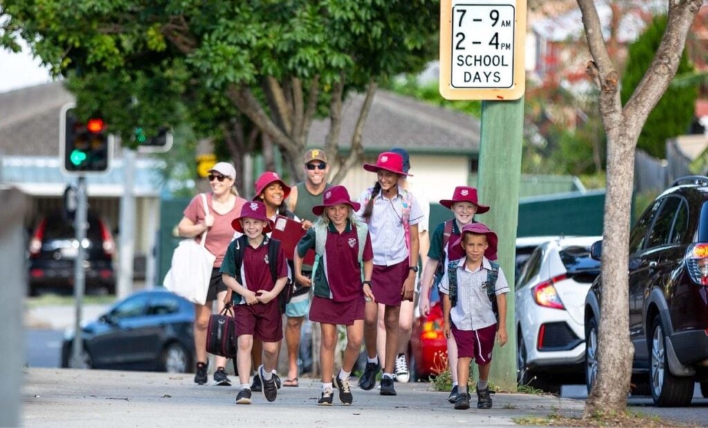 Group of school children walking with adults along local street to school