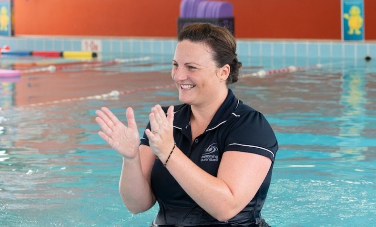 Aqua English Project: A smiling woman clapping her hands while standing in the pool of an indoor aquatic centre