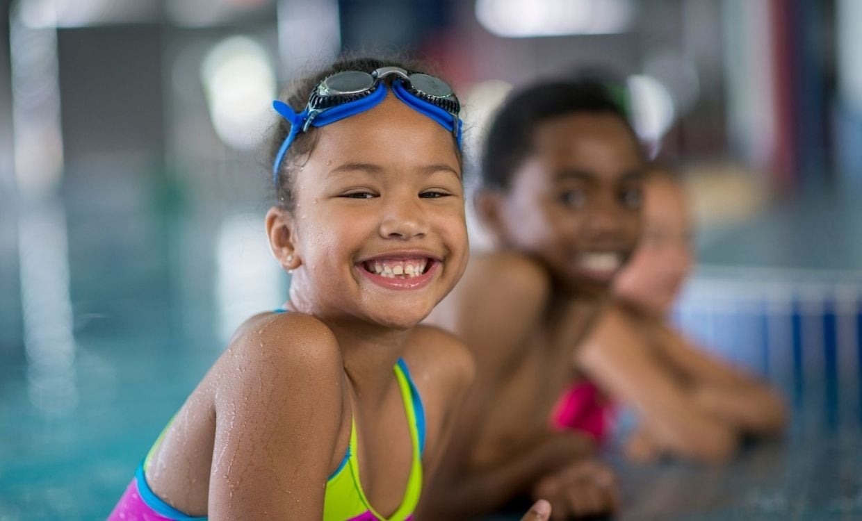 Close up of children smiling while leaning on the edge of an indoor swimming pool