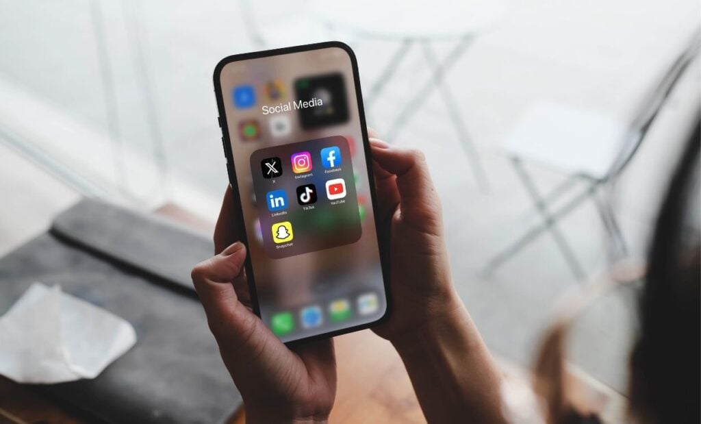 Person holding a phone with a collection of social media apps on screen