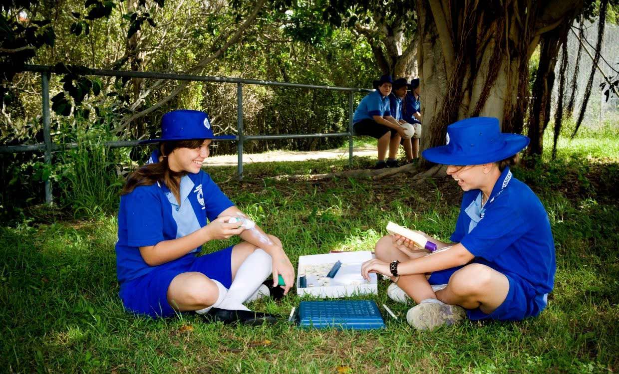 Two schoolgirls wearing sun-safe clothing and applying sunscreen while enjoying an outdoor game together