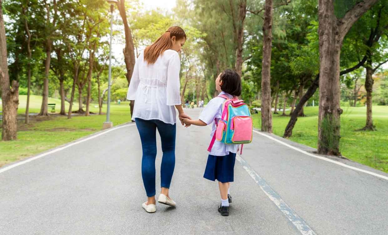 Woman and primary school student holding hands walking outside