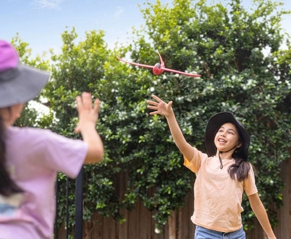 Two young happy girls throwing a toy plane in the backyard