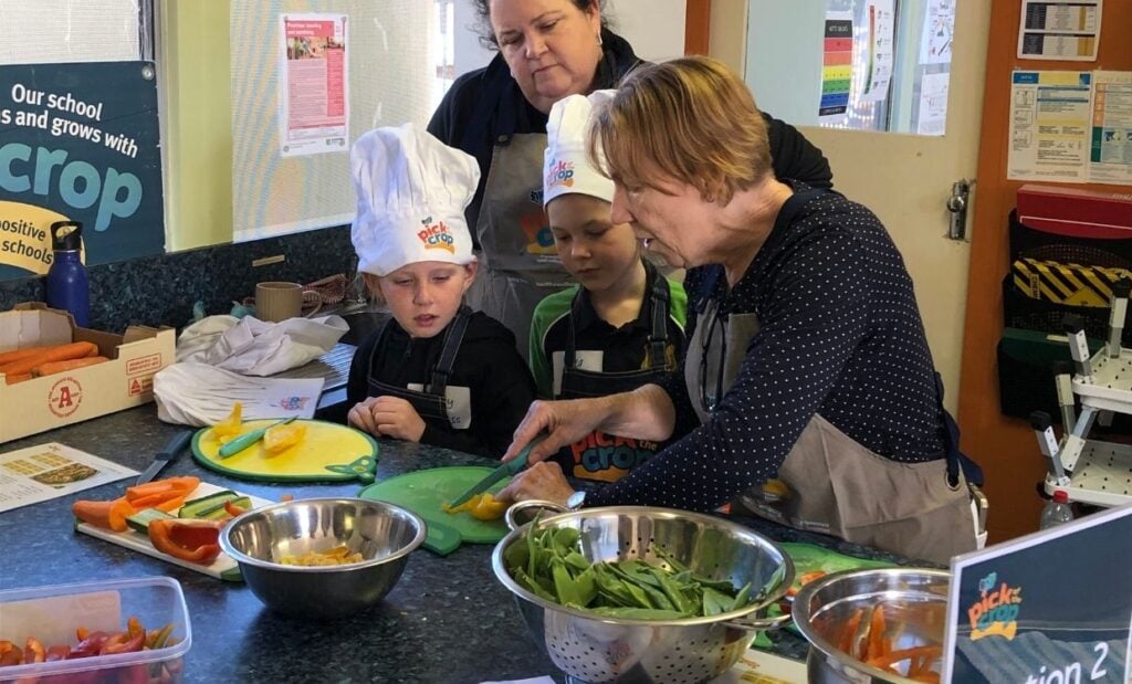 Teacher shows children how to cut up vegetables in school kitchen