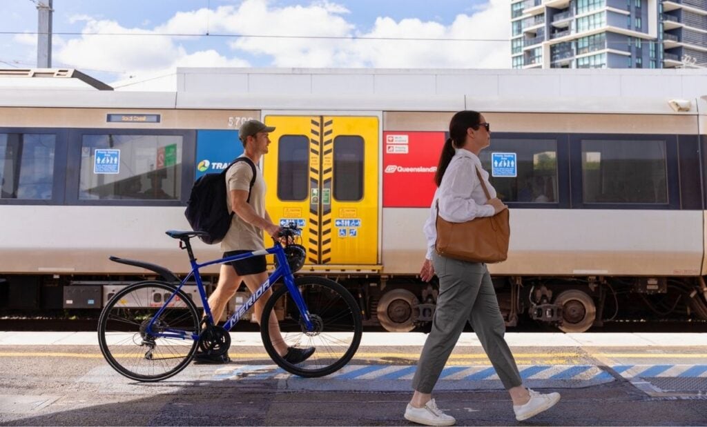 Woman walking with handbag and man walking with his bike along a train station platform.