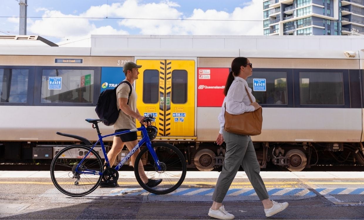 Woman walking with handbag and man walking with his bike along a train station platform.
