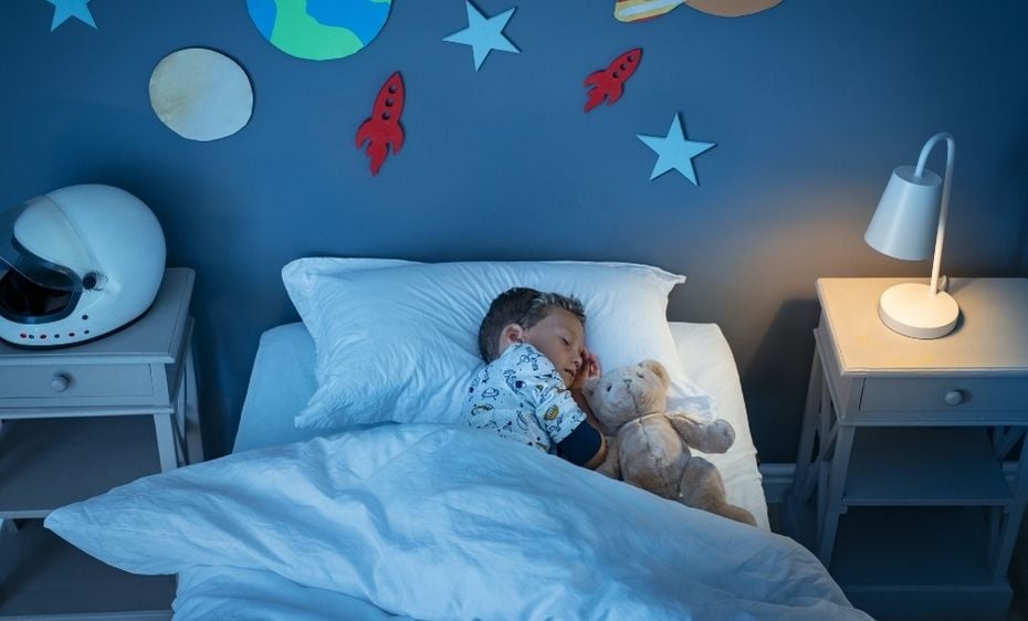 Young child sleeps in his bed hugging teddy