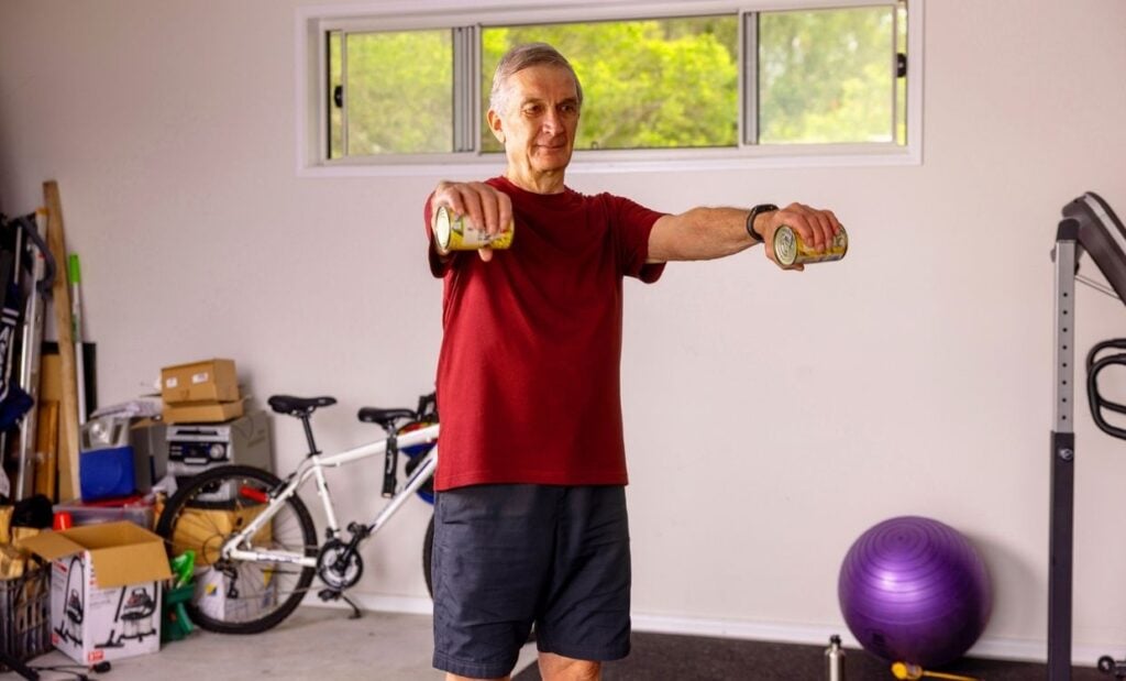 Older adult does arm raises with tinned food in home workout