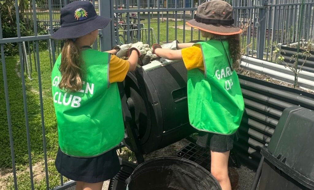 Two school girls add garden compost to composting bin