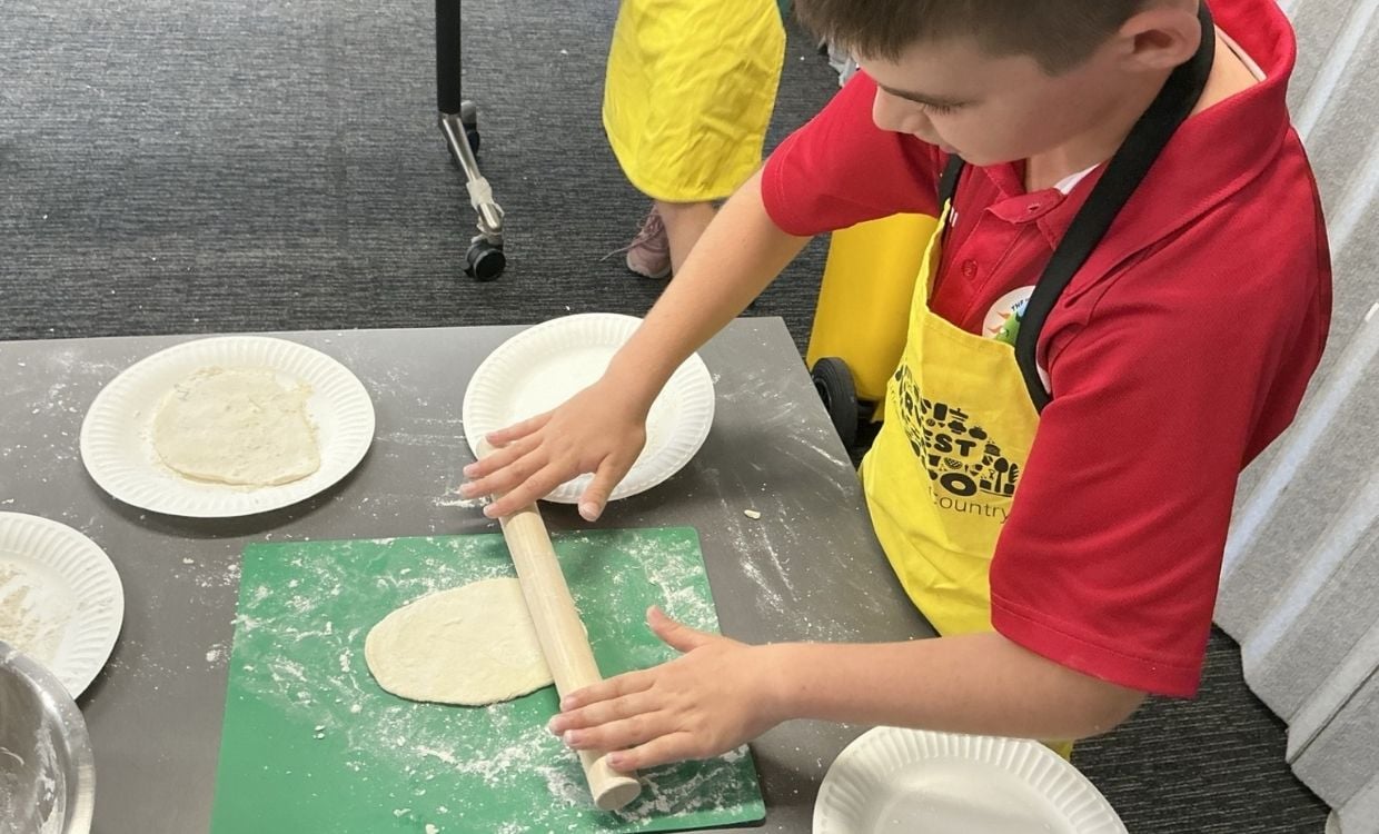 School kid rolls out dough in school kitchen