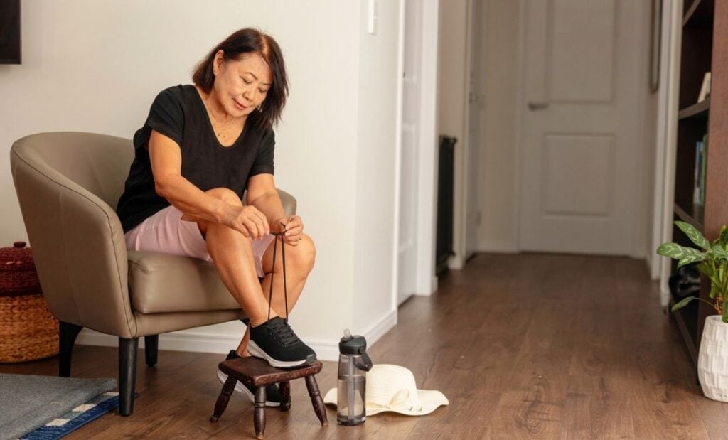 Older woman sits in a chair tying her shoelaces ahead of going on a walk
