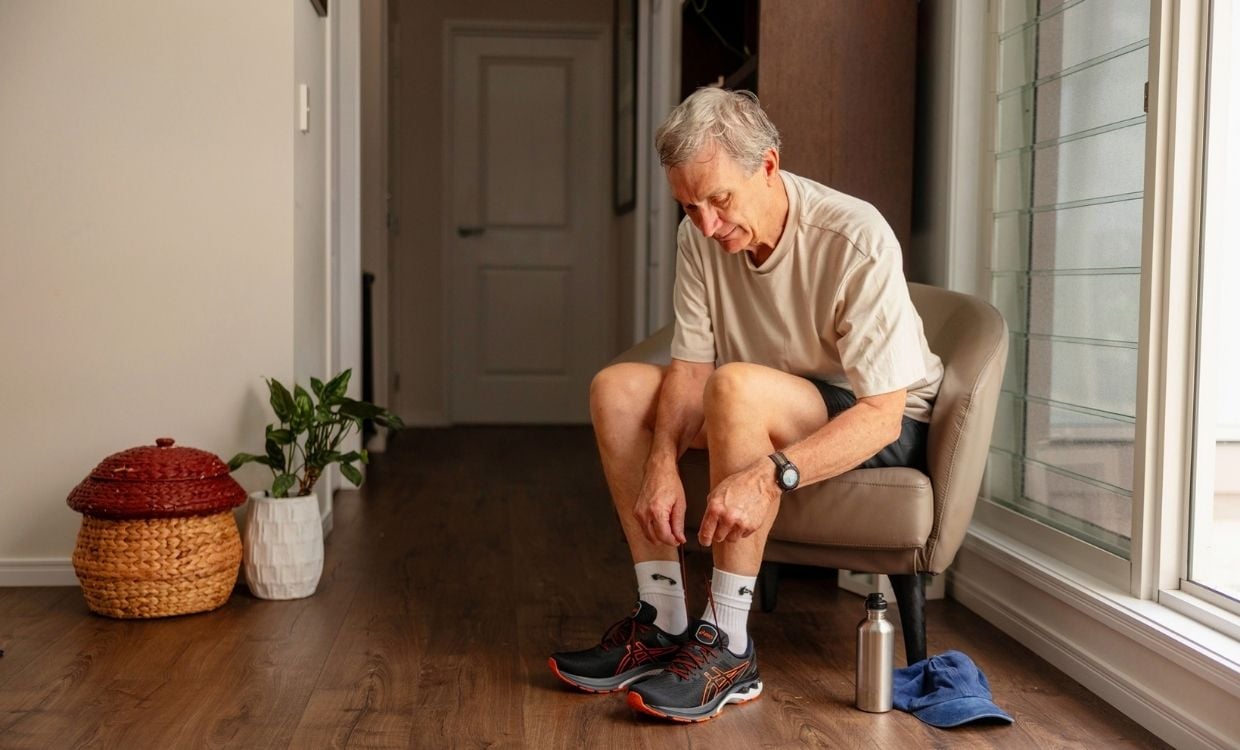 Older man sits down and ties shoelaces to prepare for physical activity