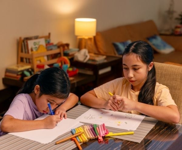 Two young girls colouring in at the dining table to wind down for bedtime