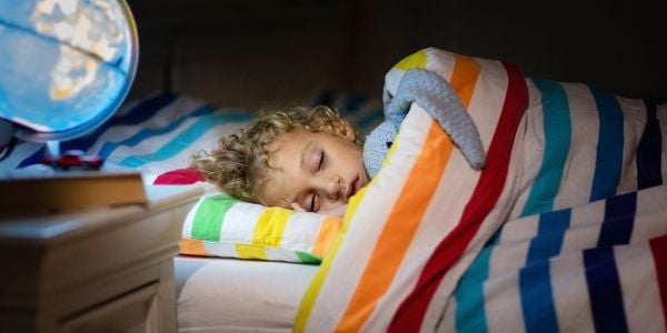 Young child asleep in bed, cuddling a toy, with a glowing World Globe nightlight on the bedside table