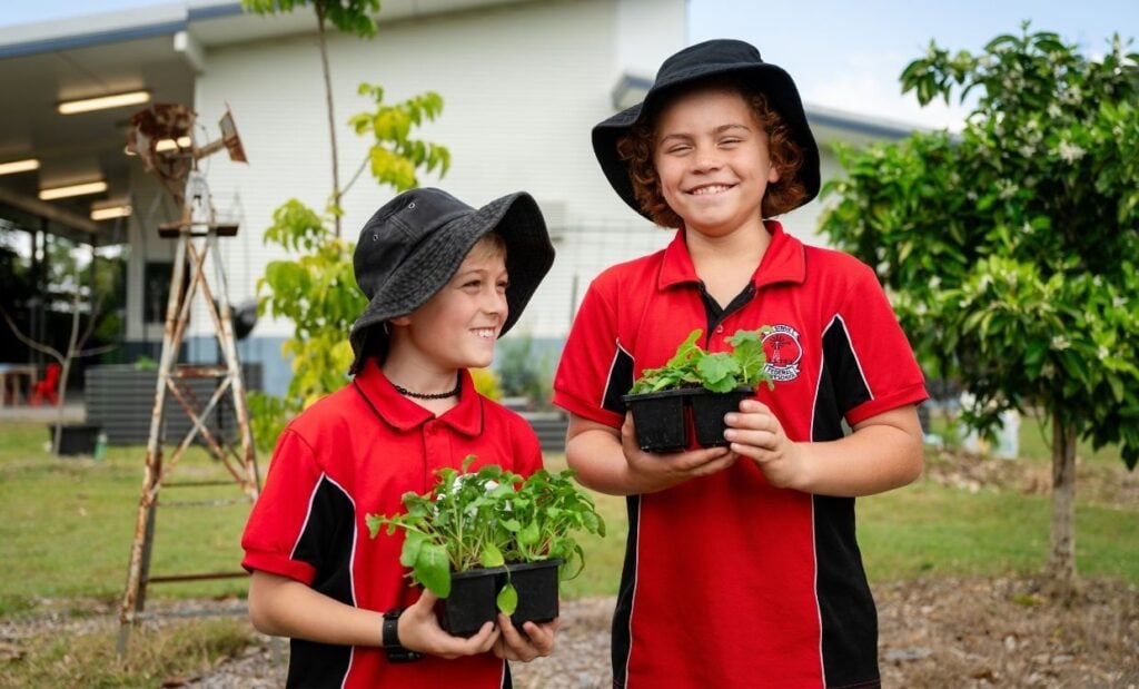 Two smiling primary school students holding seedlings while standing in the school garden