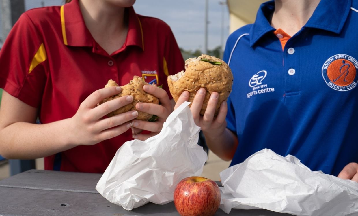 Two junior players eating healthy burgers and fruit from the canteen