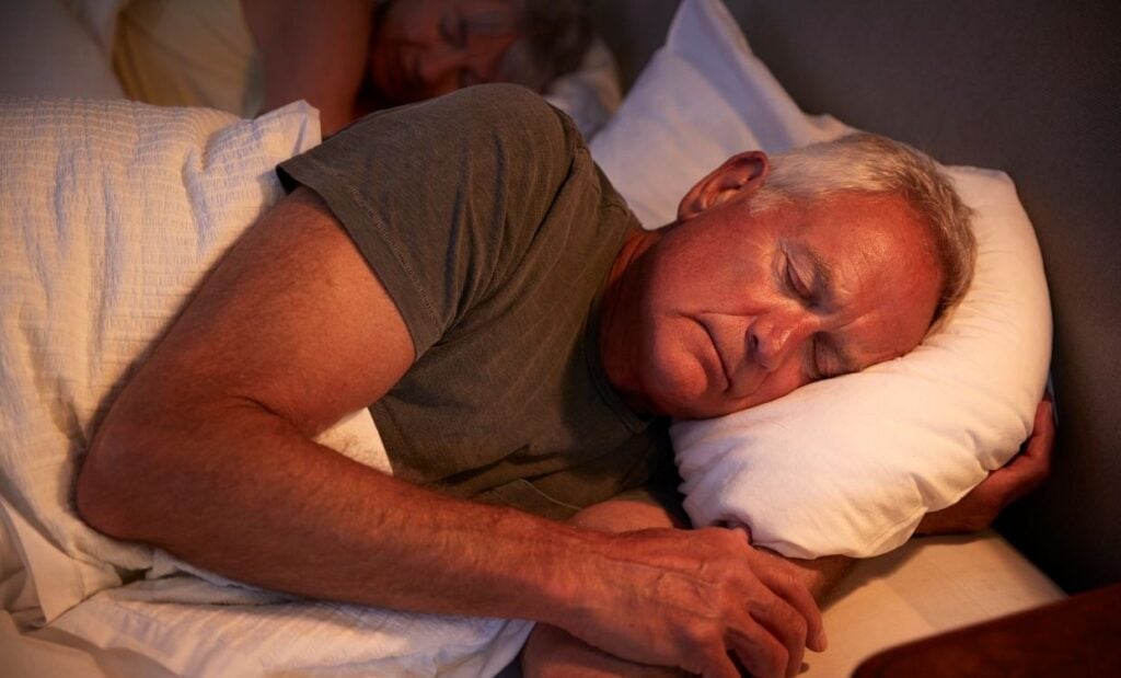 Older man and women sleep in bed